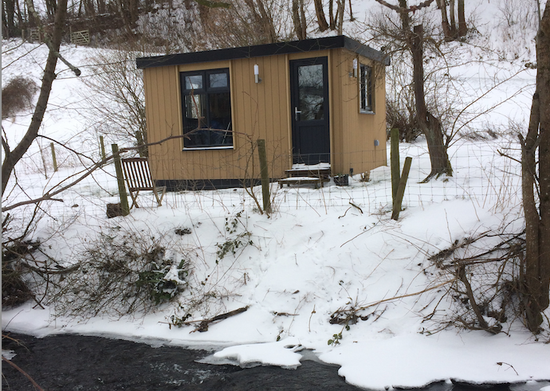 A small cabin in the snow next to a stream.